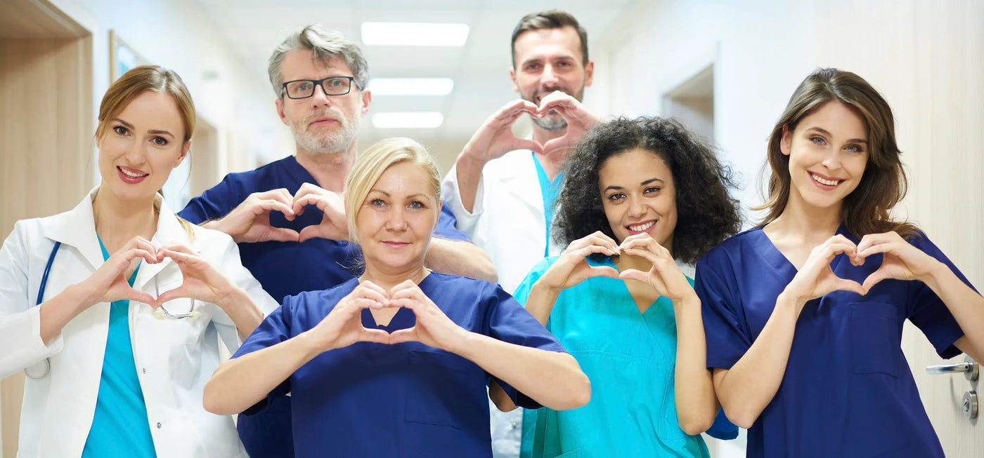 Group of essential services professionals making heart shapes with their hands in a hospital setting.