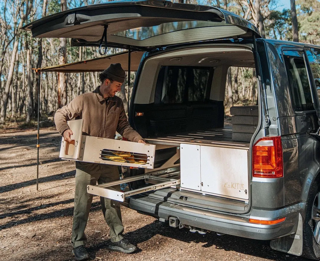 Man sets up plywood van drawer kit for outdoor camping storage in a forest setting