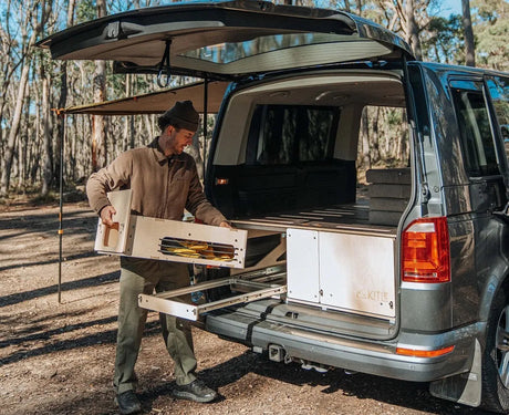 Man sets up plywood van drawer kit for outdoor camping storage in a forest setting
