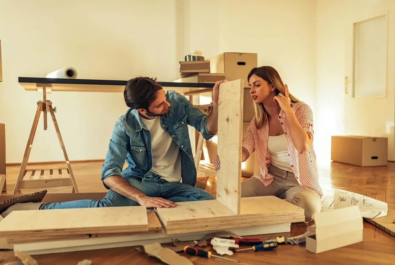 Couple assembling plywood furniture at home, surrounded by moving boxes and tools