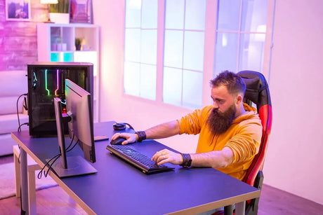 Bearded gamer sits at the wooden gaming desk in room full of neon lights