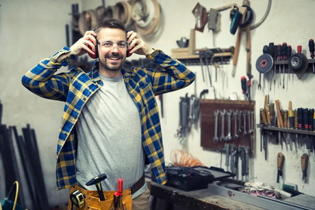 Man in workshop wearing safety gear, surrounded by woodworking tools and equipment
