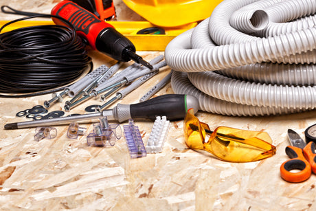 Assorted electrical tools and fittings on OSB board, including drill, conduit, and safety glasses