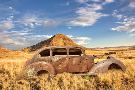 Rusty classic car in the field in front of hill