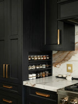 Black kitchen cabinetry made with Black Oak Timber Veneer Panel A/B UV-Coated with gold handles and a built-in spice rack, set against a white and brown marble backsplash.
