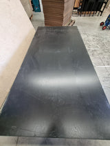 Flat black stained plywood sheet on a concrete floor with cardboard boxes in the background